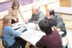 Photo of adults talking around a table stacked with papers