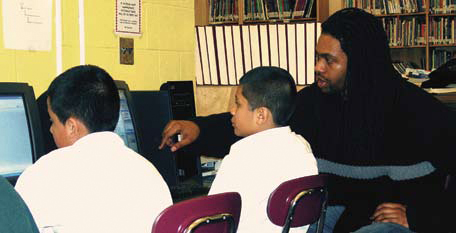 Photo of a teacher pointing out something on a computer to two students.